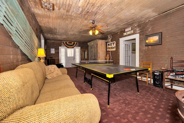 recreation room featuring wooden walls, dark colored carpet, ceiling fan, and wooden ceiling