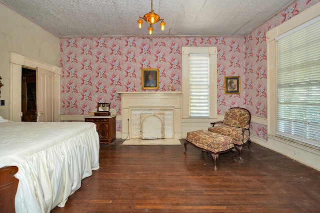 bedroom featuring a textured ceiling, an inviting chandelier, dark hardwood / wood-style flooring, and a brick fireplace