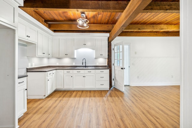 kitchen featuring white cabinets, beam ceiling, light wood-type flooring, and sink