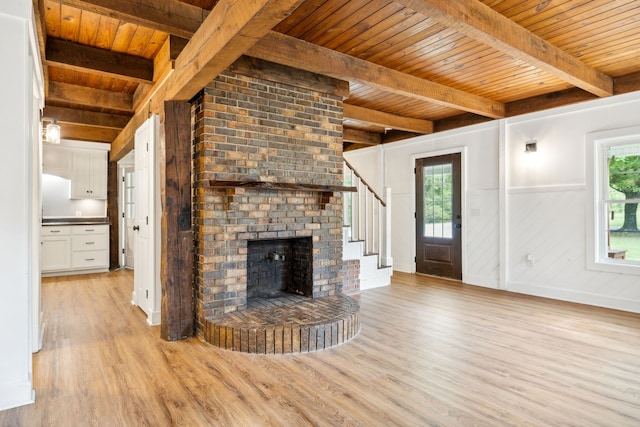 unfurnished living room featuring a brick fireplace, light wood-type flooring, beam ceiling, and wooden ceiling