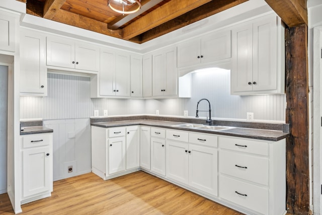 kitchen with beam ceiling, light wood-type flooring, white cabinetry, and sink