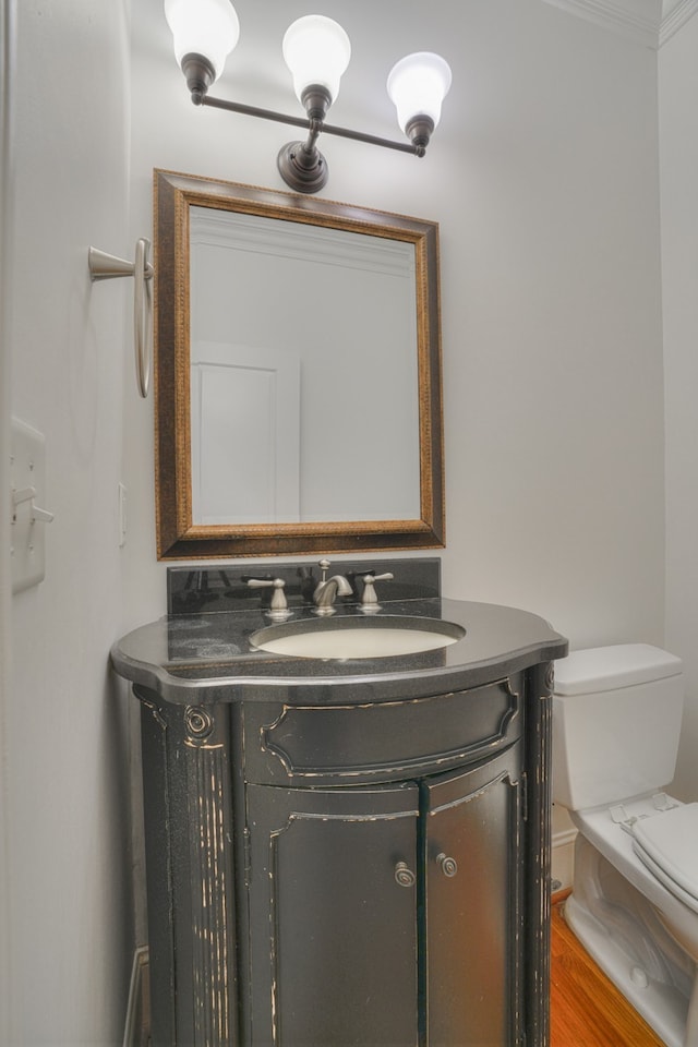 bathroom with wood-type flooring, crown molding, vanity, and toilet