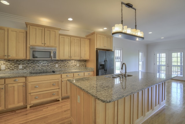 kitchen featuring hanging light fixtures, light hardwood / wood-style floors, a center island with sink, sink, and black fridge