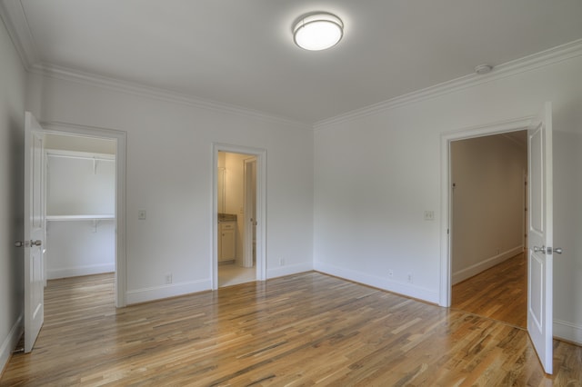 unfurnished bedroom with light hardwood / wood-style flooring, crown molding, a closet, and a spacious closet