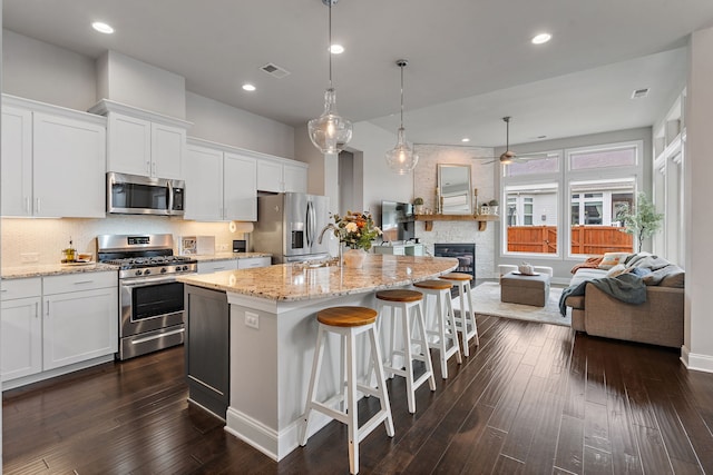 kitchen featuring a center island with sink, stainless steel appliances, white cabinetry, and a large fireplace