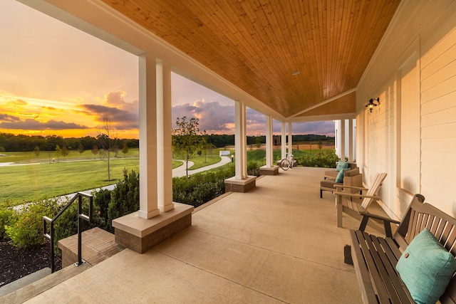 patio terrace at dusk featuring a lawn and covered porch