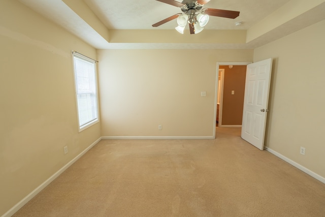 carpeted spare room featuring a tray ceiling and ceiling fan