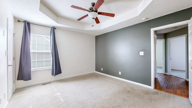 spare room featuring a textured ceiling, ceiling fan, a tray ceiling, and light hardwood / wood-style flooring