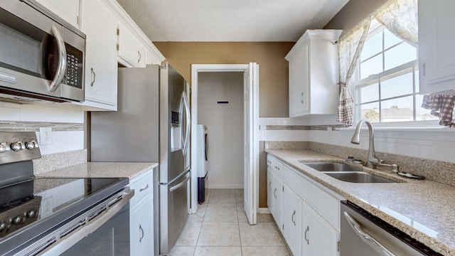 kitchen featuring stainless steel appliances, sink, light tile patterned floors, and white cabinetry