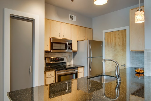 kitchen with dark stone countertops, backsplash, light brown cabinets, stainless steel appliances, and decorative light fixtures