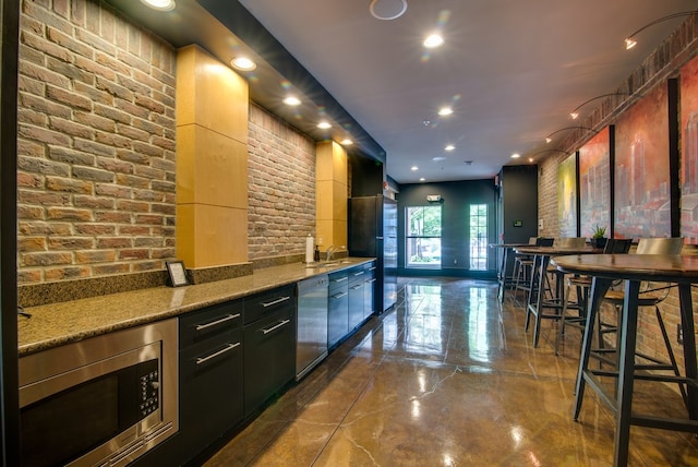 bar featuring brick wall, sink, stainless steel appliances, and light stone counters