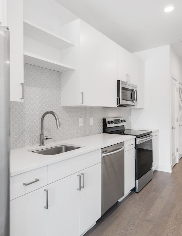 kitchen with sink, white cabinetry, light hardwood / wood-style flooring, stainless steel appliances, and decorative backsplash