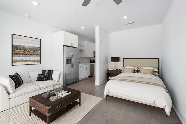 bedroom with ceiling fan, connected bathroom, sink, dark wood-type flooring, and stainless steel refrigerator with ice dispenser