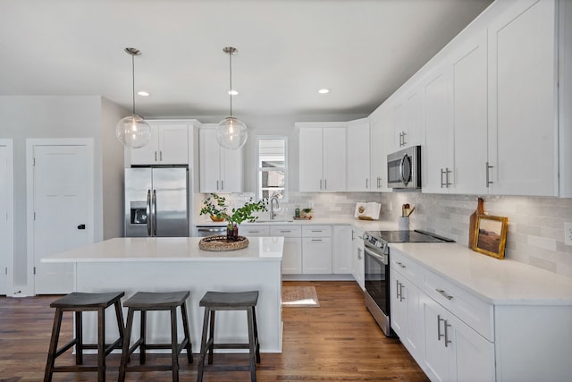 kitchen featuring white cabinets, a center island, appliances with stainless steel finishes, and dark wood-type flooring