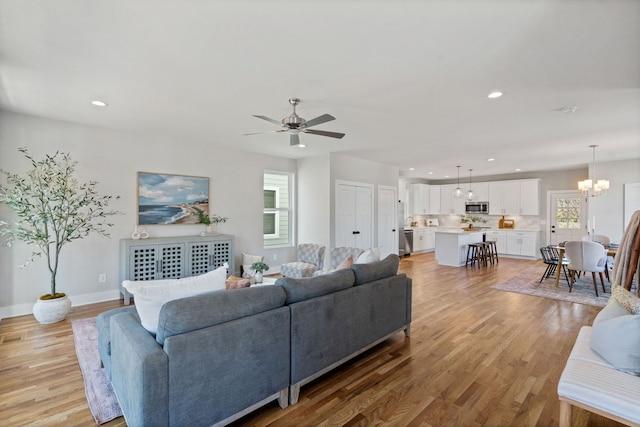 living room featuring ceiling fan with notable chandelier and light wood-type flooring