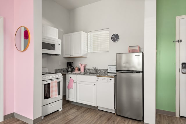 kitchen with sink, white appliances, stone counters, white cabinetry, and hardwood / wood-style flooring