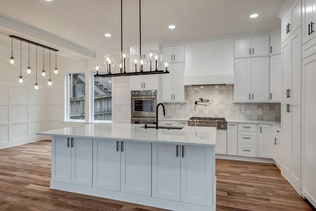 kitchen with light hardwood / wood-style floors, a large island with sink, sink, and white cabinetry