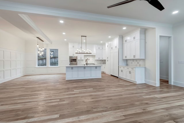 kitchen with light hardwood / wood-style floors, tasteful backsplash, white cabinets, ornamental molding, and stainless steel oven