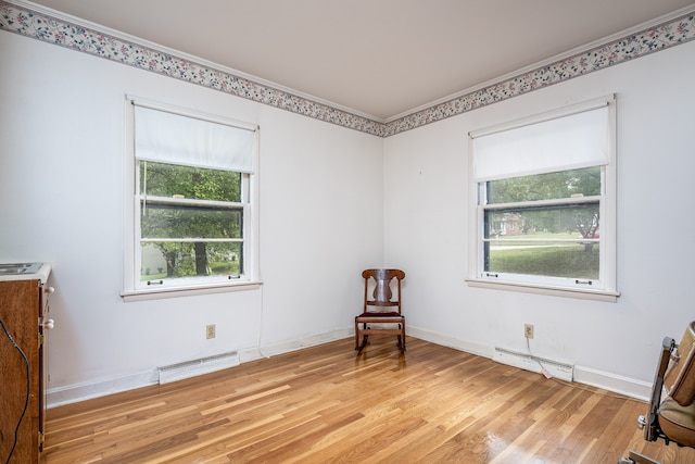 living area featuring light wood-type flooring, ornamental molding, a baseboard heating unit, and plenty of natural light