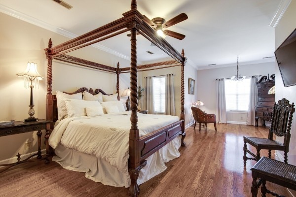 bedroom with ceiling fan with notable chandelier, multiple windows, hardwood / wood-style flooring, and ornamental molding