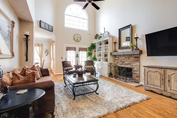 living room with light wood-type flooring, a fireplace, a towering ceiling, and ceiling fan