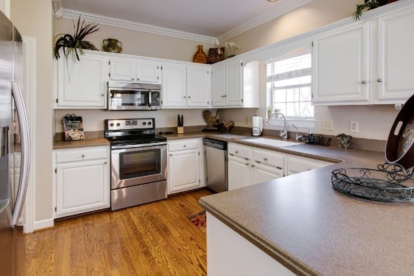 kitchen with sink, white cabinets, light hardwood / wood-style flooring, appliances with stainless steel finishes, and crown molding