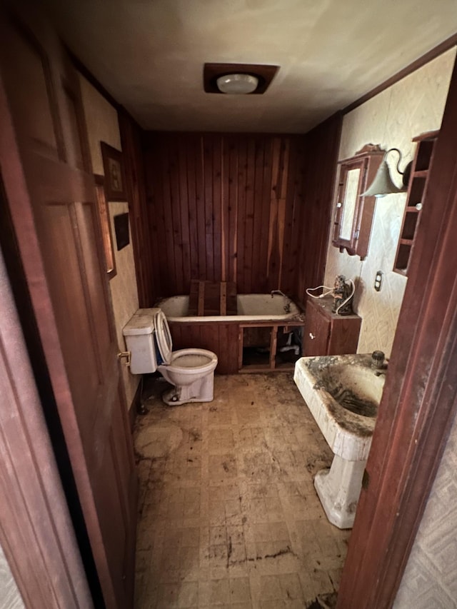 bathroom featuring toilet, wood walls, and a bath