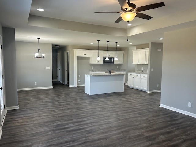 kitchen with white cabinetry, dark hardwood / wood-style floors, pendant lighting, and an island with sink