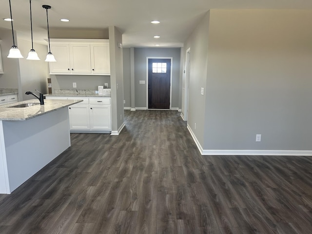 kitchen with sink, white cabinets, light stone counters, hanging light fixtures, and dark wood-type flooring