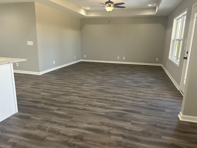 spare room with a raised ceiling, ceiling fan, and dark hardwood / wood-style flooring