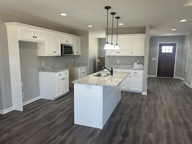 kitchen with sink, white cabinetry, light stone counters, a center island with sink, and pendant lighting