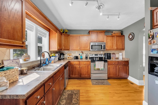 kitchen featuring appliances with stainless steel finishes, decorative backsplash, light wood-type flooring, and sink