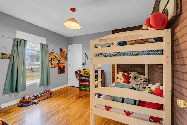 bedroom with brick wall and hardwood / wood-style flooring