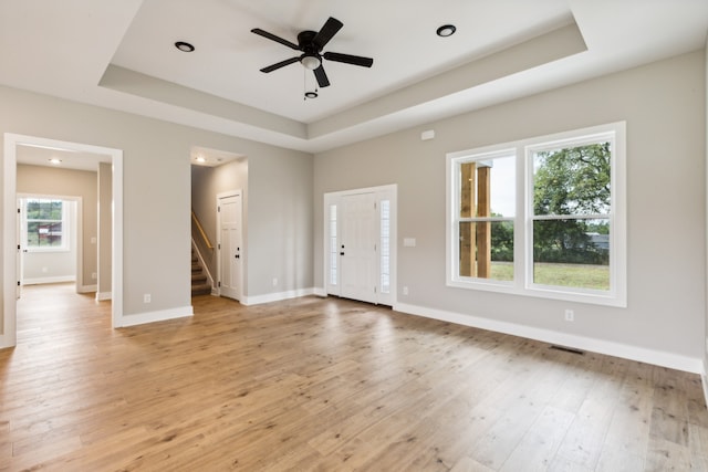 empty room featuring a tray ceiling, light hardwood / wood-style flooring, and a wealth of natural light