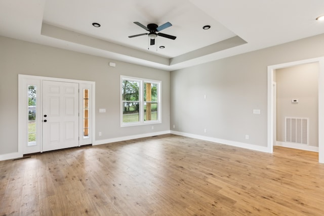 foyer with light hardwood / wood-style floors, a raised ceiling, and ceiling fan