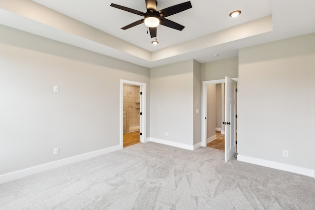 unfurnished bedroom with a tray ceiling, light carpet, and ceiling fan