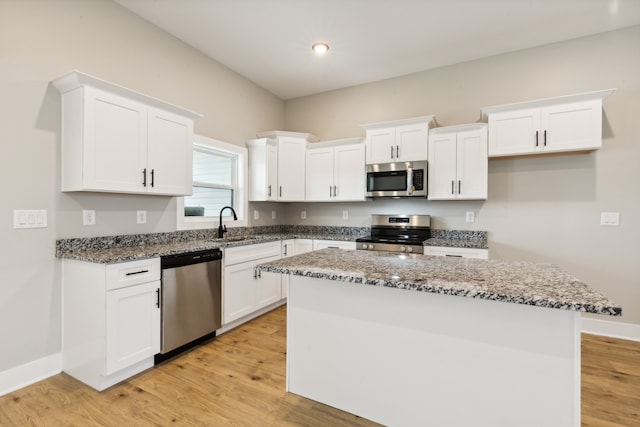 kitchen featuring appliances with stainless steel finishes, white cabinetry, a kitchen island, light hardwood / wood-style flooring, and dark stone counters