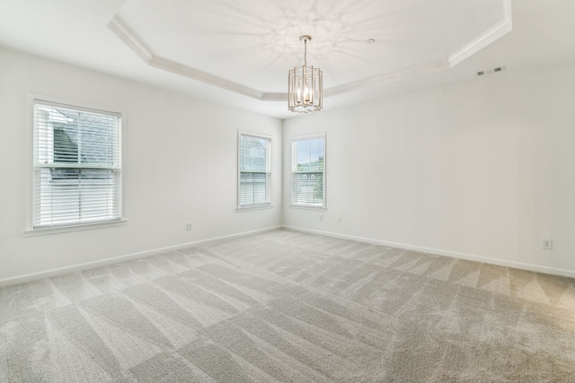 carpeted empty room with a notable chandelier, a tray ceiling, and crown molding