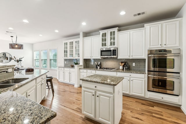 kitchen with decorative light fixtures, a kitchen island, stainless steel appliances, and white cabinetry