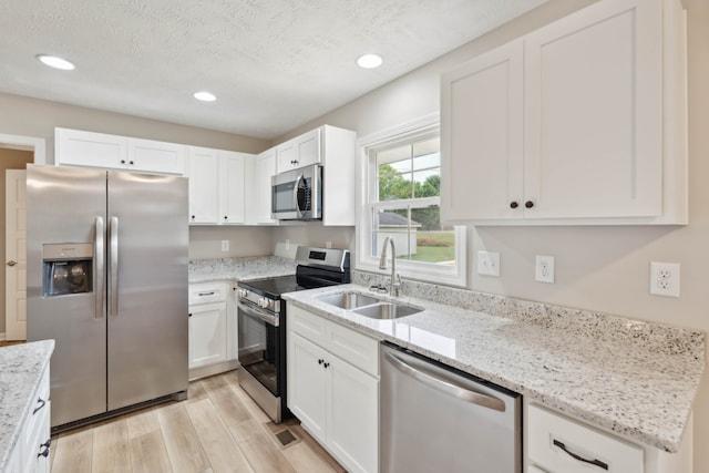 kitchen with appliances with stainless steel finishes, white cabinets, a textured ceiling, light hardwood / wood-style flooring, and sink