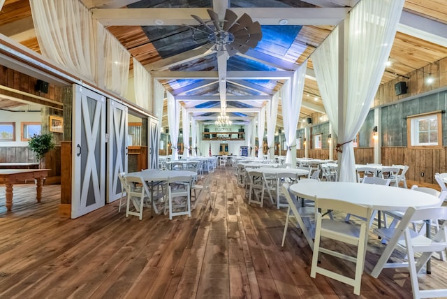 dining room featuring lofted ceiling with beams, wood-type flooring, wood walls, and ceiling fan