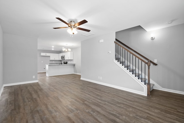 unfurnished living room featuring ceiling fan with notable chandelier and dark hardwood / wood-style flooring