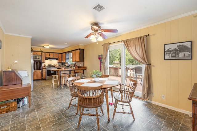 dining room featuring ceiling fan, wood walls, and ornamental molding