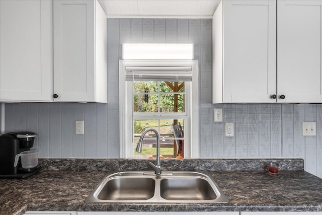 kitchen with dark stone countertops, wood walls, sink, and white cabinets