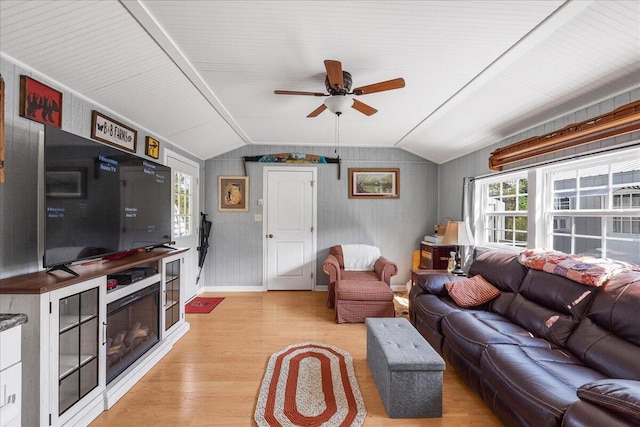 living room featuring light wood-type flooring, vaulted ceiling, ceiling fan, and wood walls