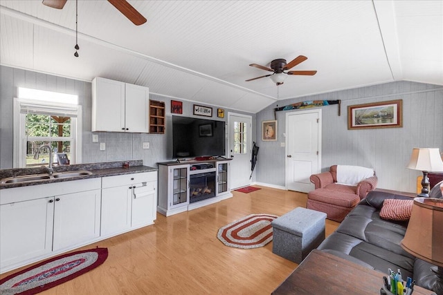 living room with ceiling fan, lofted ceiling, wood walls, sink, and light hardwood / wood-style flooring