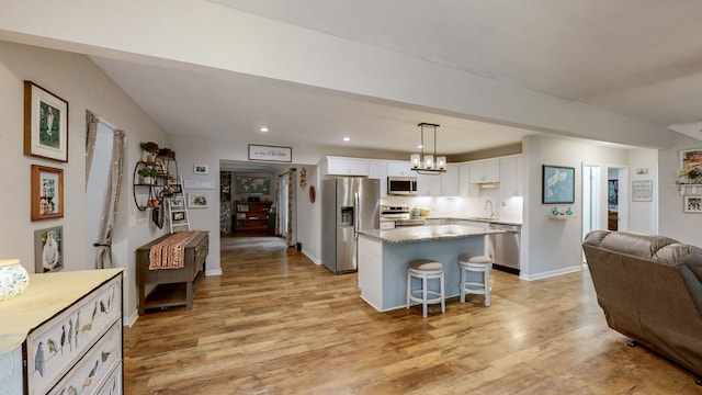 kitchen with pendant lighting, light wood-type flooring, white cabinets, a kitchen island, and stainless steel appliances