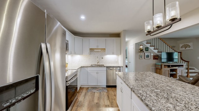 kitchen featuring light wood-type flooring, sink, white cabinetry, hanging light fixtures, and appliances with stainless steel finishes