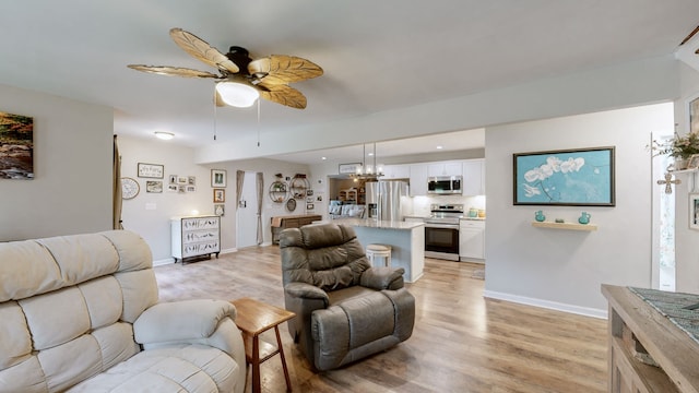 living room featuring ceiling fan with notable chandelier and light hardwood / wood-style floors