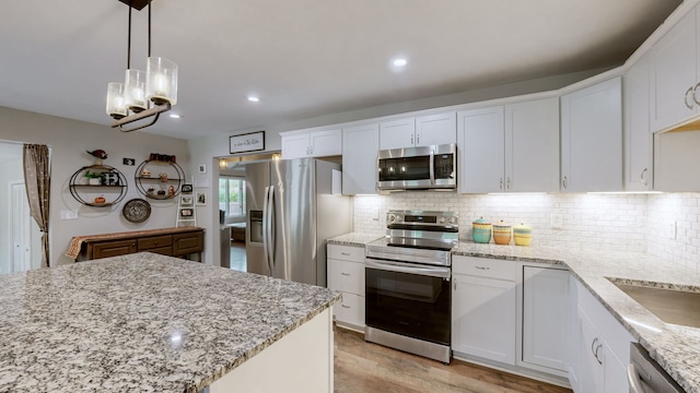 kitchen with appliances with stainless steel finishes, white cabinets, light wood-type flooring, decorative light fixtures, and a notable chandelier